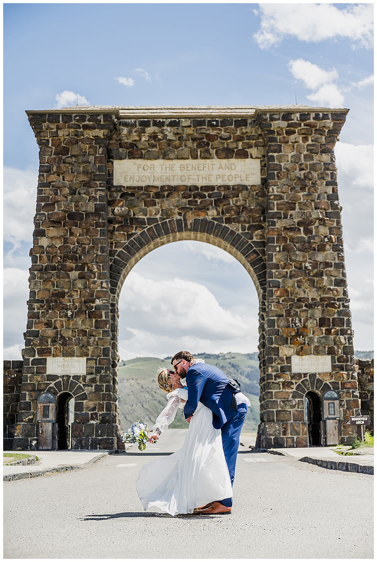 Bride and groom kissing in front of the Roosevelt Arch during an elopement in Yellowstone National Park with mountains behind them.