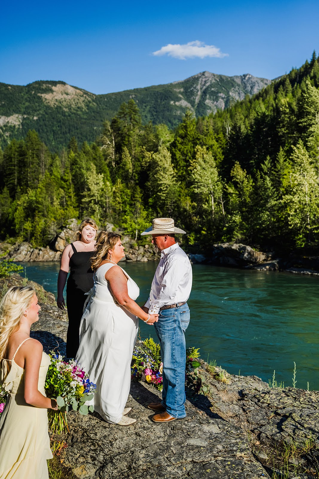 Bride and Groom at Belton Bridge in West Glacier during an elopement ceremony, with Flathead River, trees and mountains behind them.