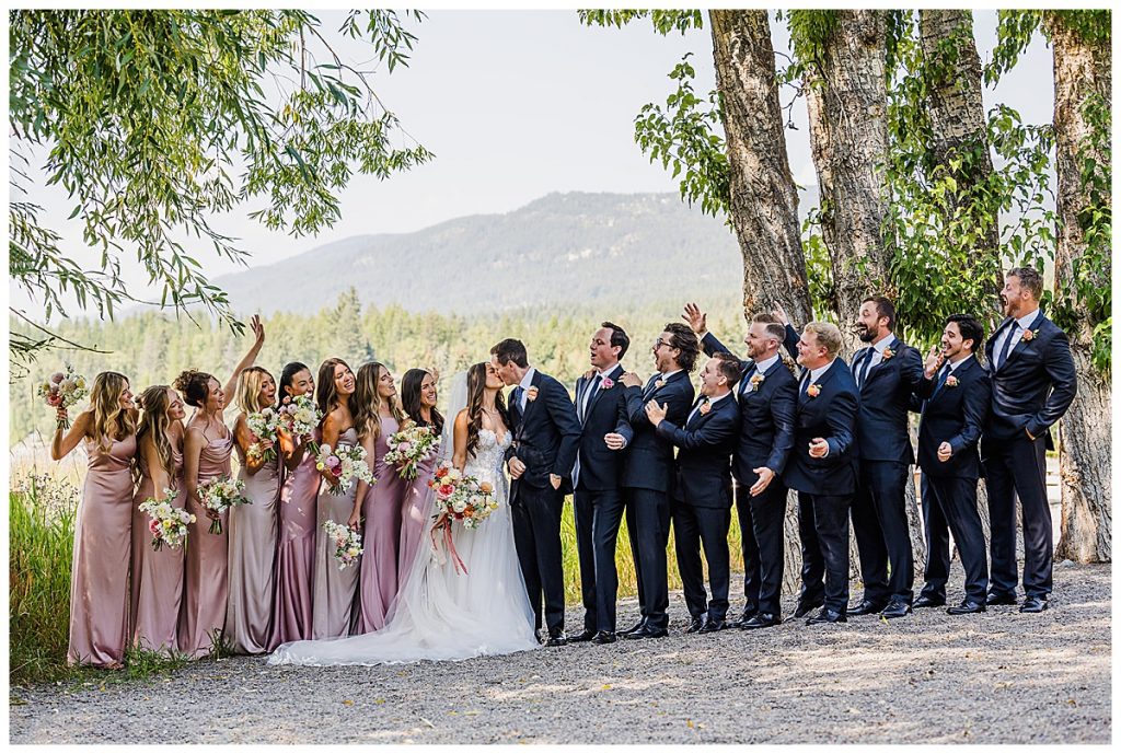 Bride and Groom kissing in the middle of a line up of their attendants at their  wedding at The Lodge at Whitefish Lake in Whitefish, MT.